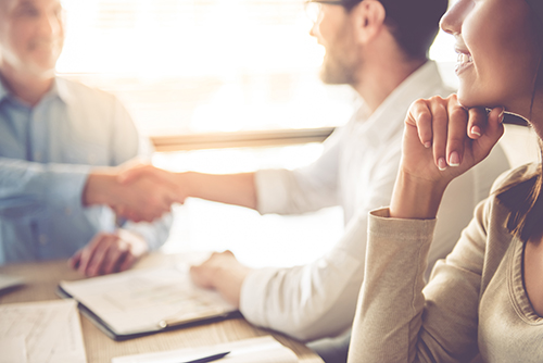 image of financial advisor sitting in front of couple at a table, shaking hands with the male